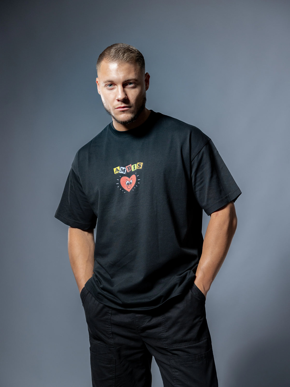 Face d'un t-shirt oversize noir Ambis avec le logo écrit d'Ambis et un cœur au centre